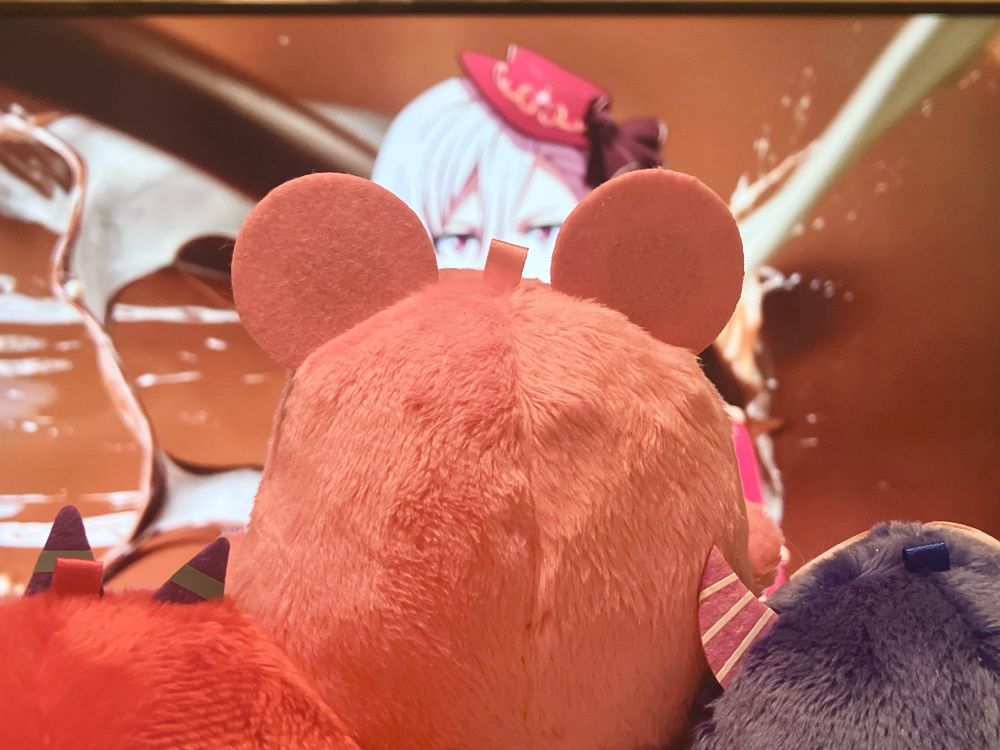 手前に、左からモンりく、モンてん、モンいおの後ろ姿がアップで写っていて、奥にテレビの大画面で写っている、地上波で流れたTRIGGERのDARSのCMが写っている。CMが九条天のシーンで、モンてんちゃんの耳の間から天くんの顔が覗ける。