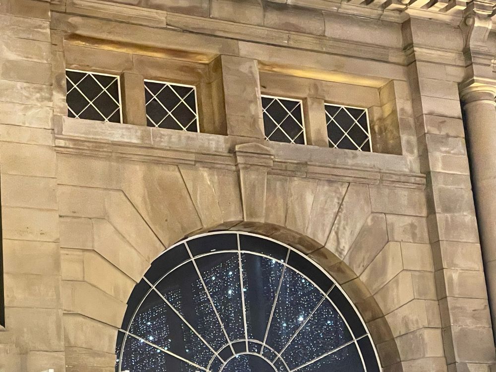 Christmas lights reflected in a semi-circular window of a stone wall with pillars. 