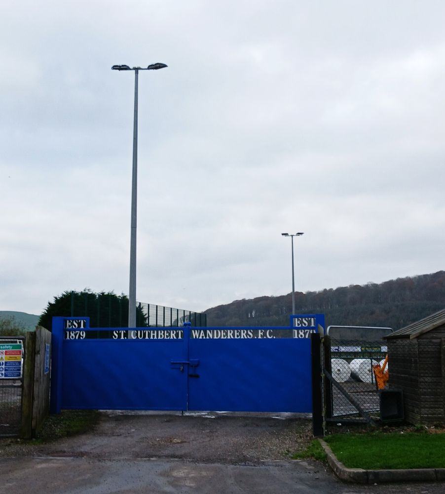 A blue gate with the words ST CUTHBERTWANDERERS EST 1879 in an unpicturesque photo.
It looks a bit like a builder's yard but the trees on the hillside beyond are more in keeping with this part of Scotland. 