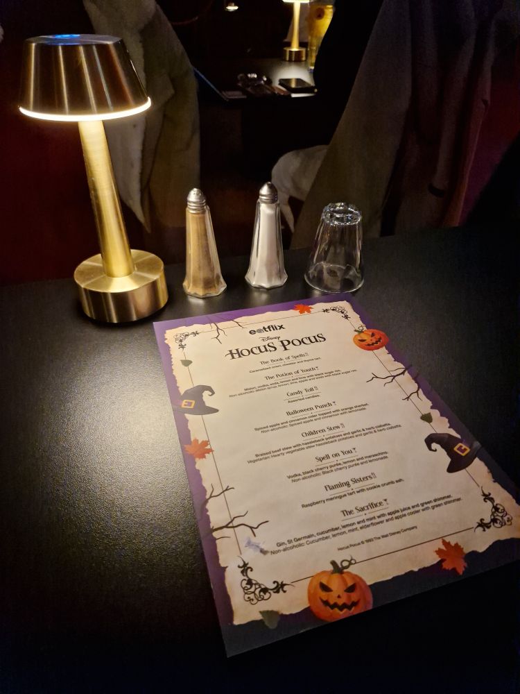 Hocus Pocus themed menu on a table, under a small lanp.