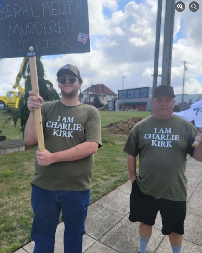2 white men wearing a green "I Am Charlie Kirk" t-shirt and holding signs. One sign reads: "Liberal Media Murdered Charlie Kirk"