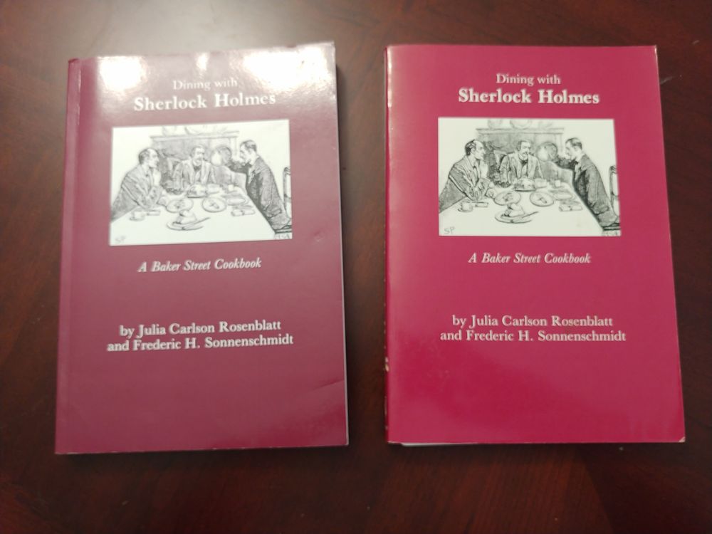 Picture of two books: 'Dining with Sherlock Holmes: A Baker Street Cookbook' by Julia Carlson Rosenblatt and Frederic H. Sonnenschmidt. Both with red covers, the book on the left a darker auburn red.