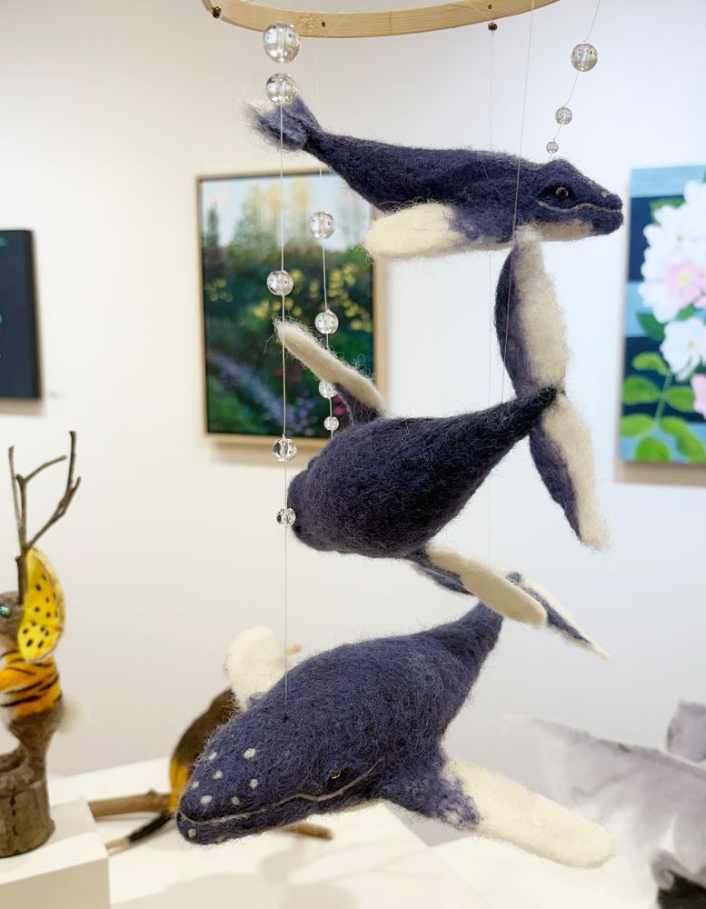 Family Photo (2025) - needle felted hanging mobile type humpback whale sculpture by Lynn Wartski.  Three blue humpback whales with white tipped fins swim through the air suspnded from a bamboo ring.  Glass bead "bubbles" rise from the creatures.