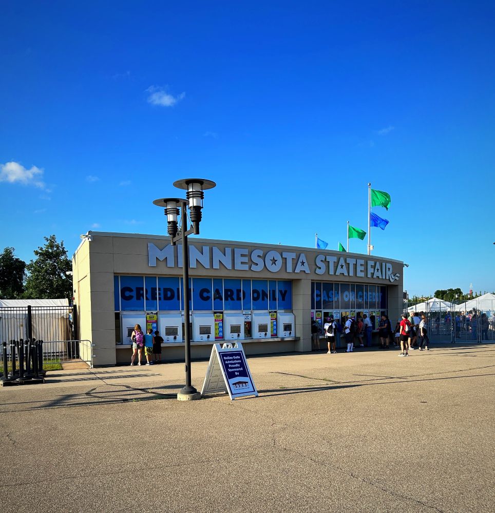 Minnesota State Fairgrounds building with green and blue flags flying against a deep blue sky.