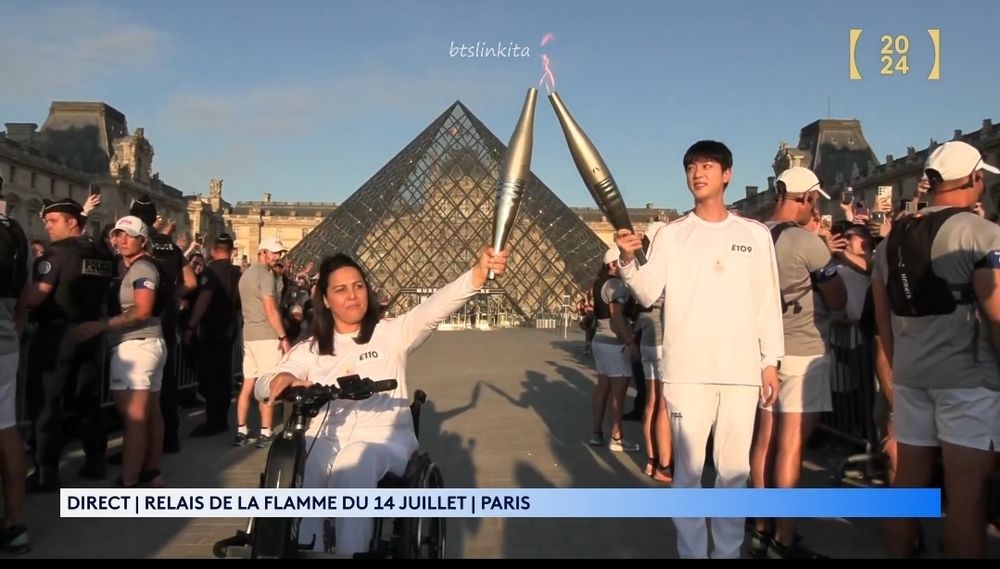 Olympic torchbearer Kim Seokjin meeting the next torchbearer in front of the Louvre Museum at the 2024 Olympics in Paris, France.