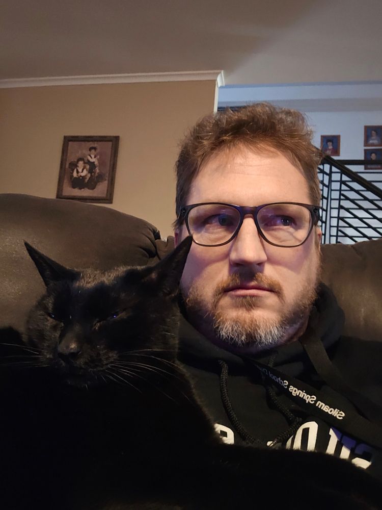 Cat and Cat Dad (human) sitting on couch annoyed at being awoken from a nap, refusing to look at the camera. 