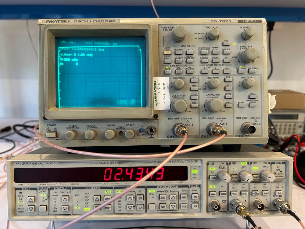 SR620 time interval counter with an oscilloscope on top of it. The scope shows a screen with frequency and other data. 