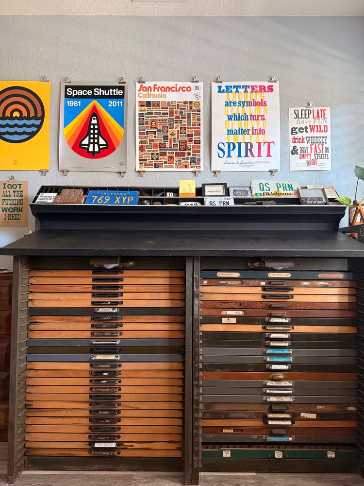 A 48-drawer type cabinet with multicolored faces and handles against a wall with posters 