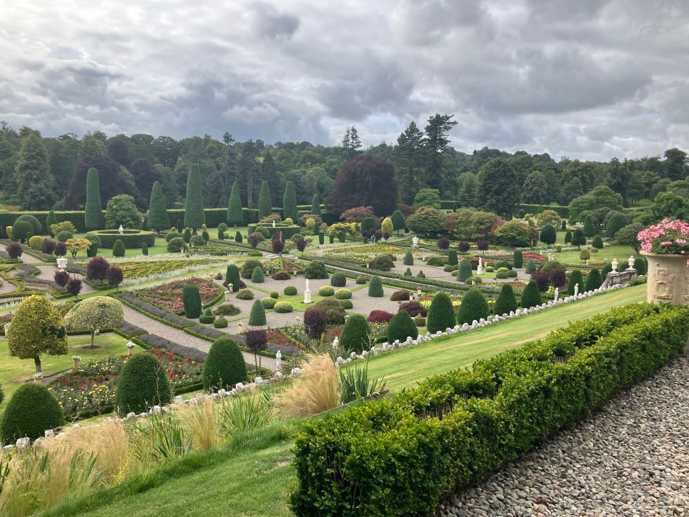 View from above a formal garden with sculpted trees and parterre hedges with grassy slopes above 