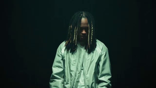 a man with dreadlocks is wearing a green jacket and a white shirt .