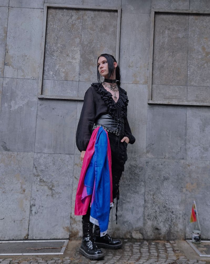 Picture of me with many chains, a black blouse and a leather corset. I have a Bi flag on my side 