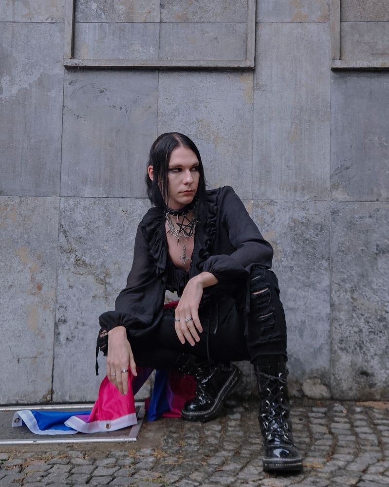 Picture of me with many chains, a black blouse and a leather corset. I have a Bi flag on my side 