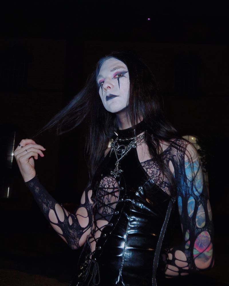 Me wearing a vinyl top and fishnets as sleeves and I am wearing leather pants that are laced on the side. I am wearing goth makeup where my face is completely white my neck black and I have spiky eyeliner. I am holding my hair to the side