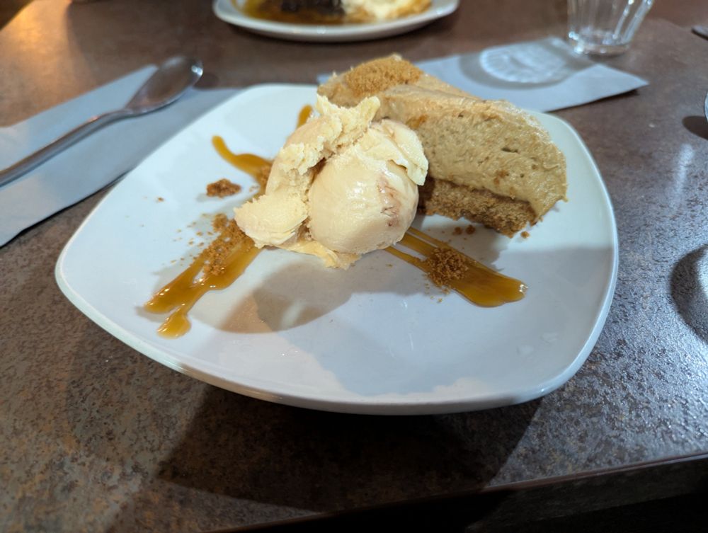 A slice of biscoff cheesecake, dusted with biscoff biscuit crumbs, alongside several scoops of salted caramel ice cream, drizzled with additional caramel sauce 