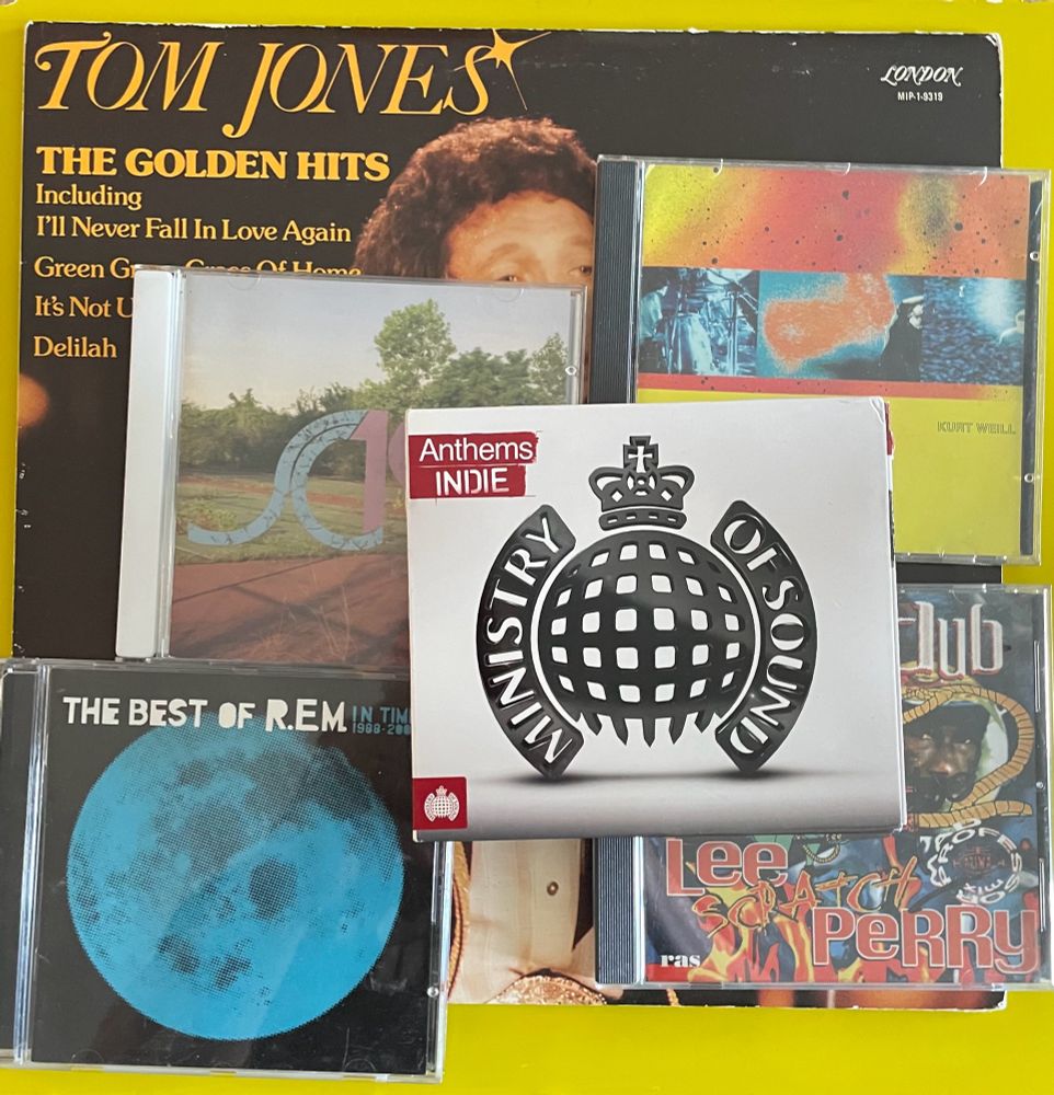 Single image on solid yellow background of one LP and five CDs purchased at a neighborhood garage sale. Includes  Tom Jones The Golden Hits LP,  and the CDs Ministry Of Sound Indie Anthems, R.E.M. The Best Of R.E.M. 1988-2003, Secretly Canadian SC100, Lee Scratch Perry and Mad Professor Fire In Dub,  The Young Gods Play Kurt Weill 