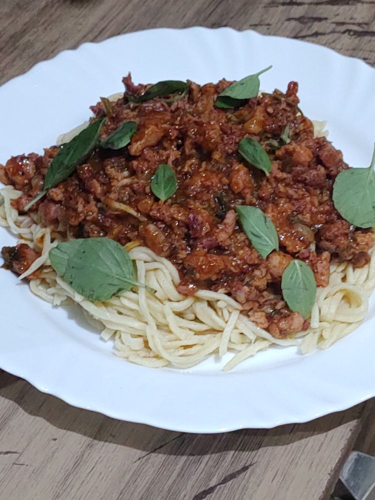 Bolonhesa de linguiça e massa fresca em um prato branco liso e raso.
