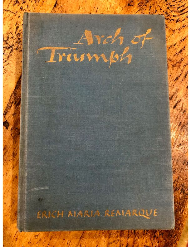 The cloth cover of a first edition of Erich Maria Remarque's Arch of Triumph (1945). The cover is a worn gray/blue, with the title and author imprinted in gold.
