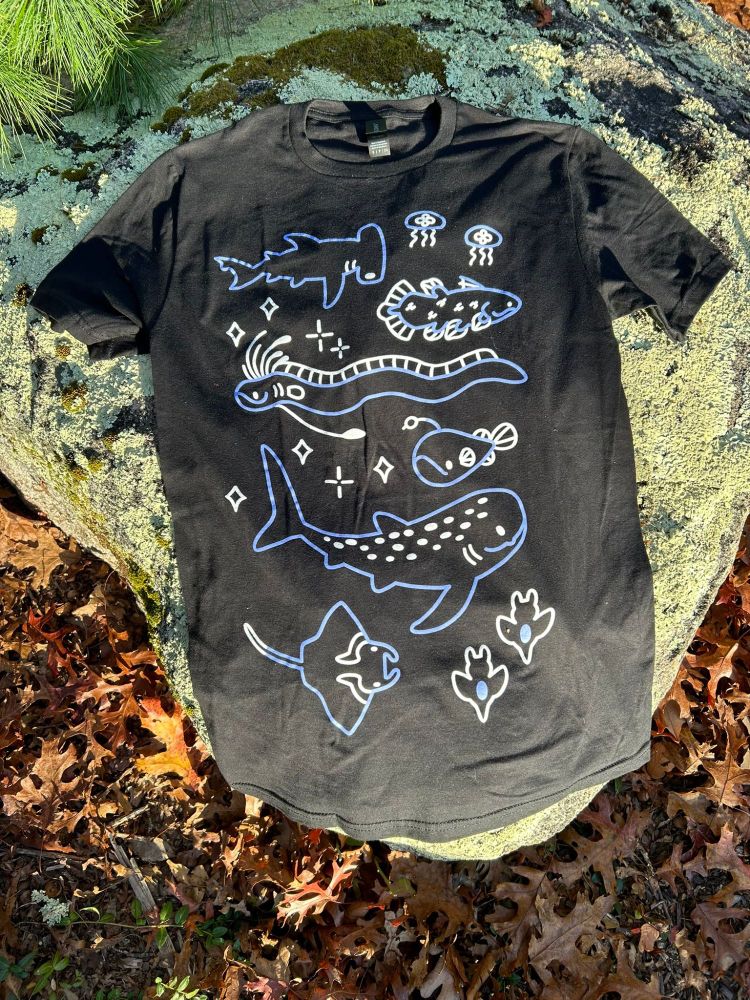 Photo of a black shirt with blue and white outline drawings of various sea creatures. The animals pictured are a hammerhead, jellyfish, coelacanth, oarfish, angler fish, whale shark, manta ray, and sea angels.