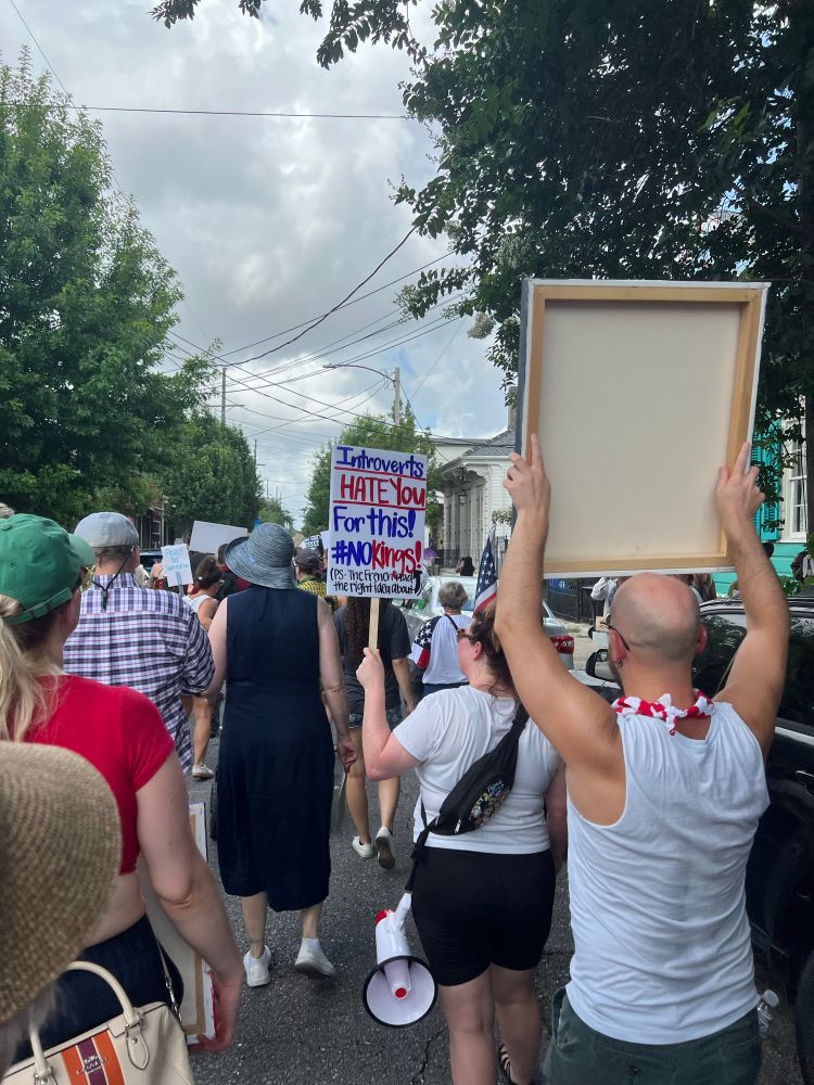 Woman in a crowd of marchers with sign reading “introverts HATE you for this! No kings!”