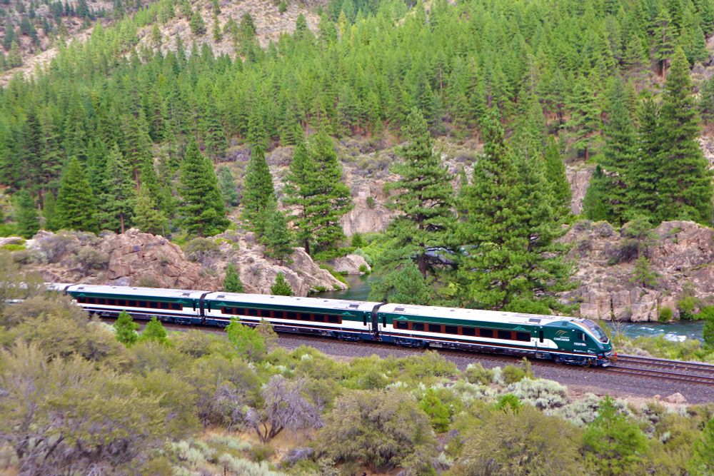 New Amtrak Cascades train after it left the factory glides through California countryside with threes and brush on the surrounding hills. 