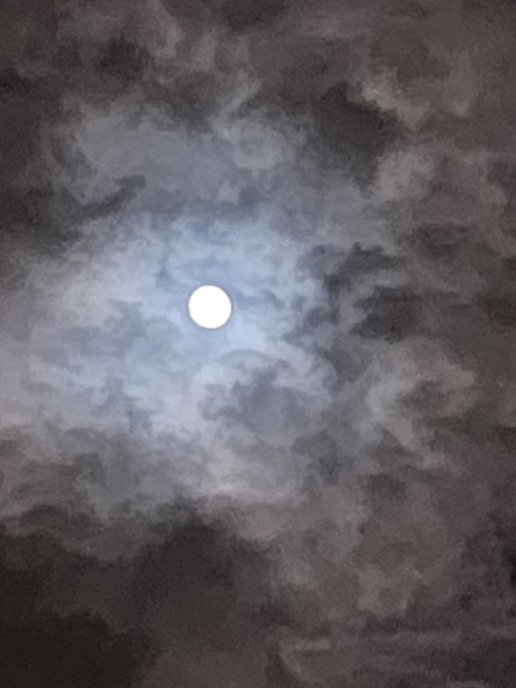 A cellphone picture of the full moon surrounded by clouds. The low lighting giving it a painted look. 
