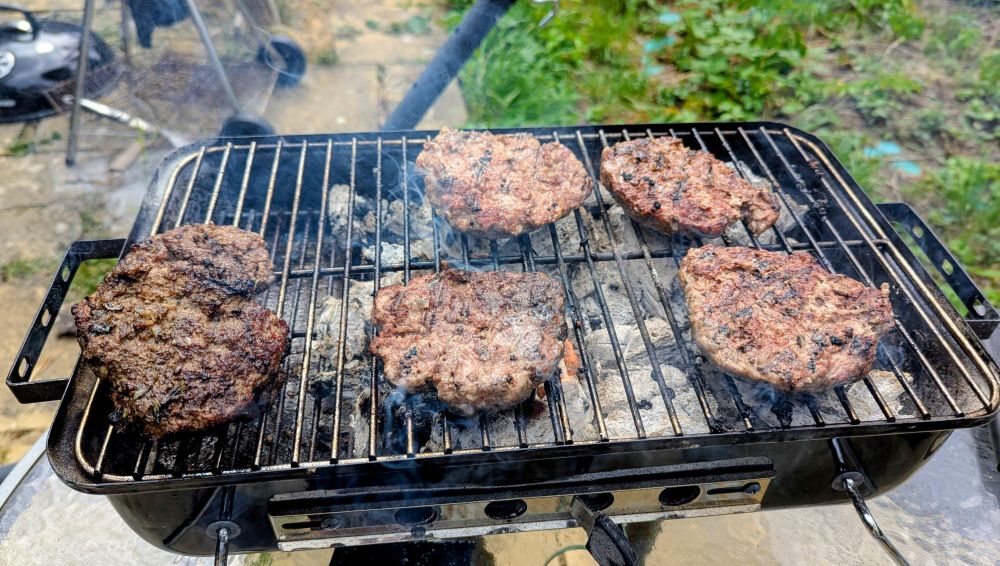 Burgers have been placed on a smaller BBQ and are being grilled