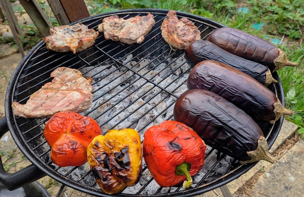 Pork shoulder steaks, peppers and aubergines are laid on the edge of a lit BBQ