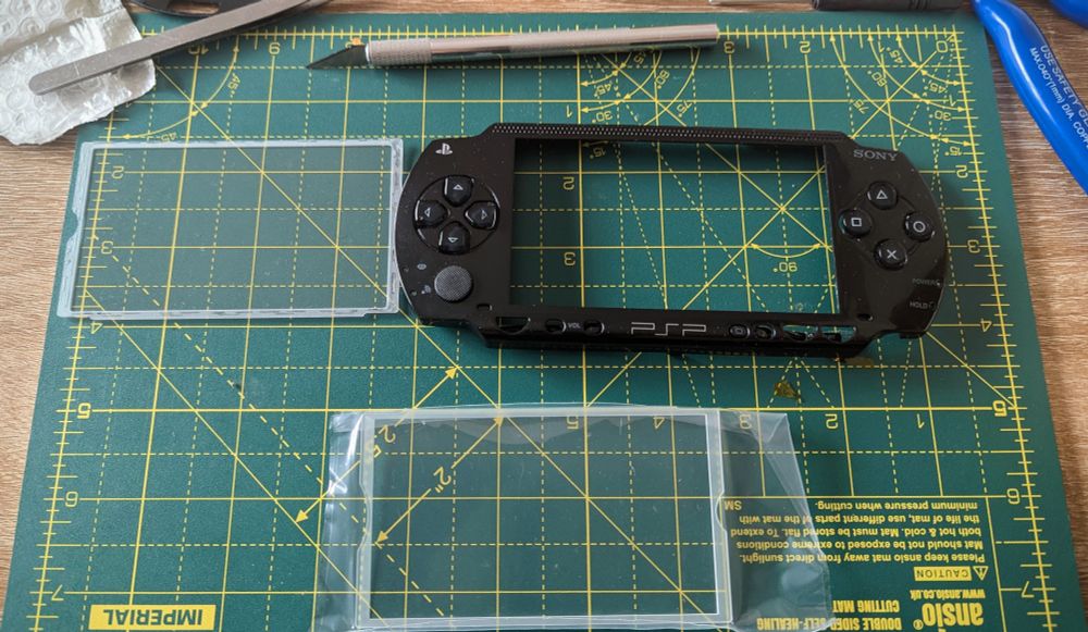 A PSP faceplate with its lens taken out. On the bottom center is the glass lens replacement.