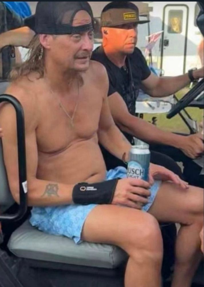 Kid Rock is shirtless in the passenger seat of a golf cart, holding a can of Busch Light and wearing a backwards hat, just a sad sack of bones with a vacant stare