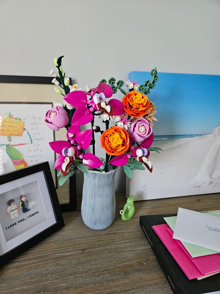 A vase filled with Lego flowers sitting on a shelf. 