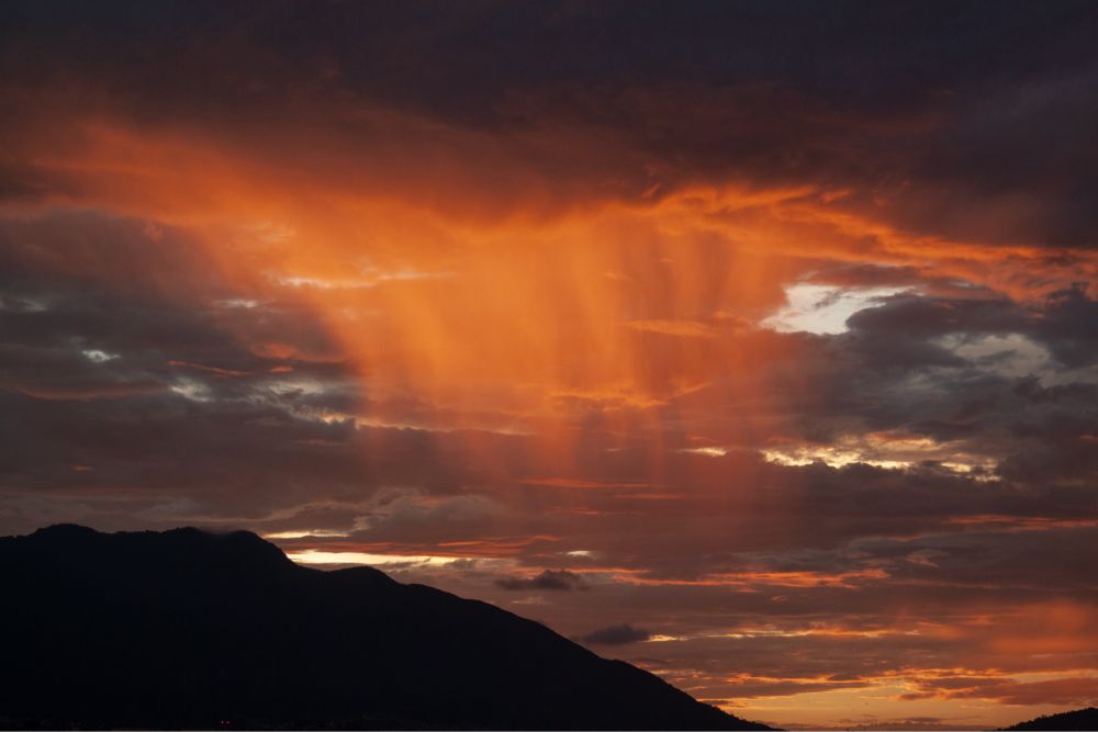 Rain shafts over Kathmandu at sunset, with the rain columns illuminated by the orange light.