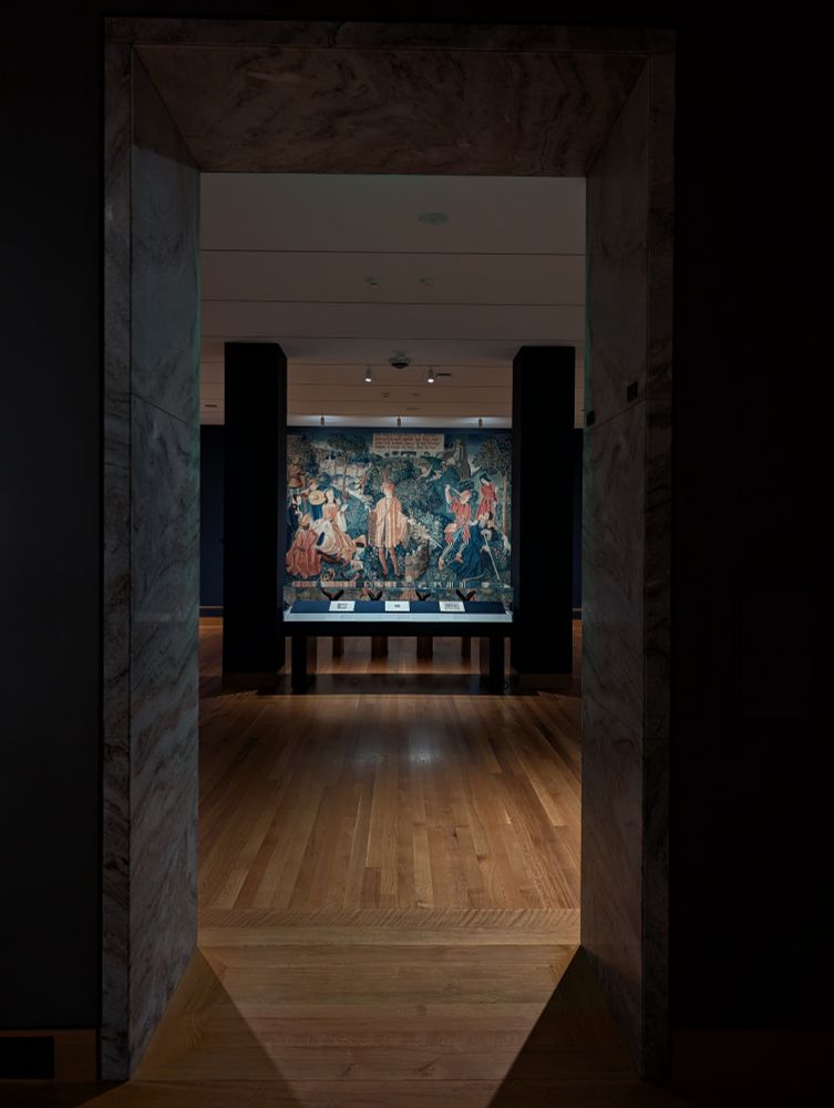 Photo taken through a doorway at the Cleveland Museum of Art, which leads into Gallery 113, French Tapestries and Illuminated Manuscripts. The 16th century French tapestry "Time" from the Chateau de Chaumont set is visible on the far wall, and there is a display case in front of it containing four opened Books of Hours.