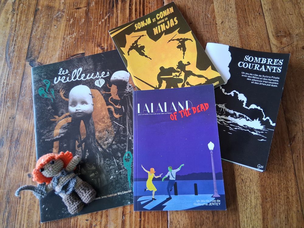 Une photo de mes 4 livres de jdr : Sonja et Conan conter les Ninjas, Les Veilleuses, Lalaland of the Dead et Sombres Courants... et une poupée Sonja faite au crochet