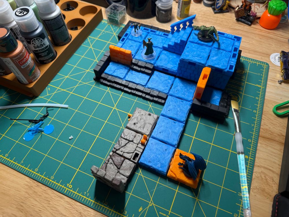 A small dungeon made up of individual 1x1 tiles. Mostly blue with some black and a couple orange pieces thrown in as well. General desk detritus can be seen throughout. 