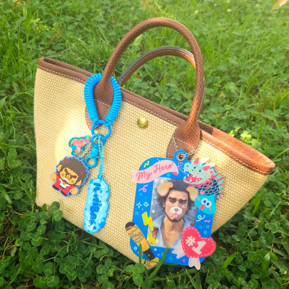 Ichiban rubber keychain, Nancy keychain, and Ichiban puffy name tag attached to a carabiner and spring wristlet hanging off of a purse handle. On the other end of the same purse handle, there's an Ichiban themed photocard holder with a dog filter Ichiban photocard inside. Designs are inspired by Yakuza 7/Like a Dragon and oshikatsu photocard decorations.