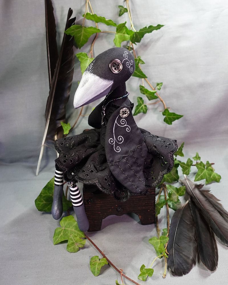 a crow art doll with button eyes in black dress with striped legs