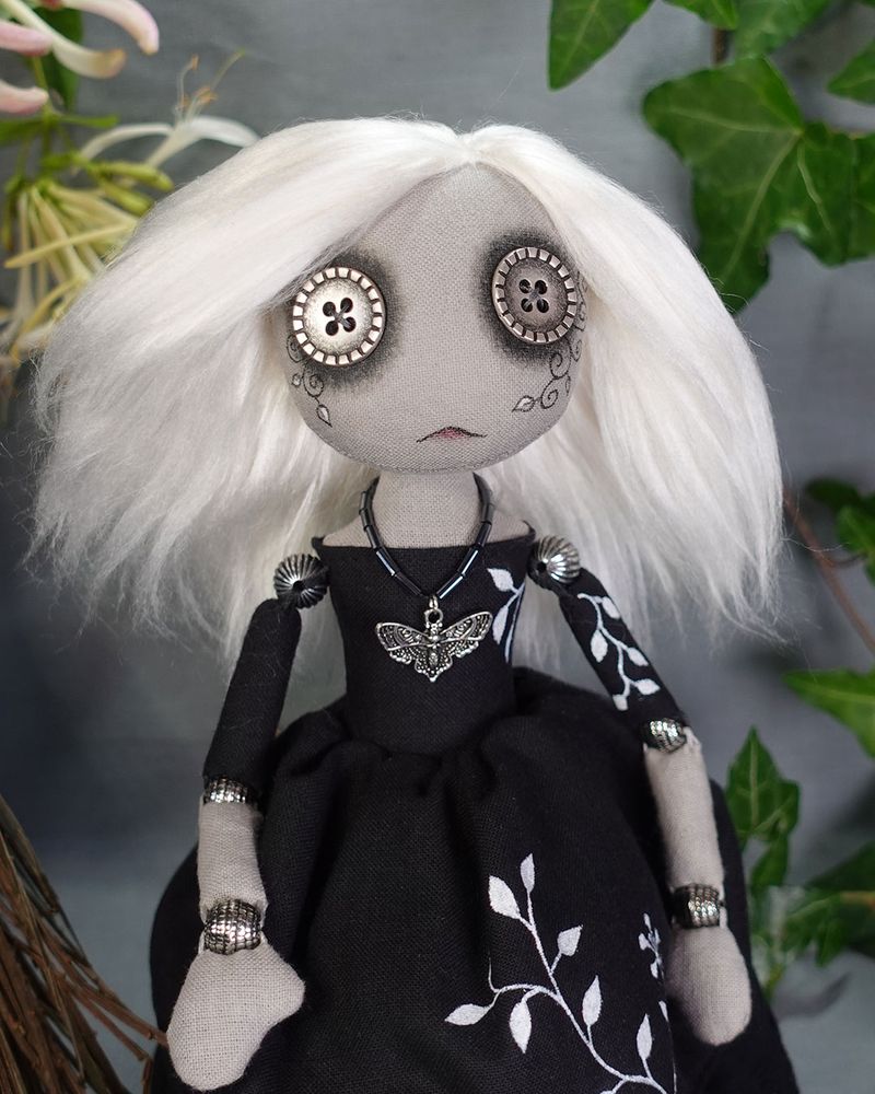 gothic doll with white hair and pale button eyes. Face and dress are painted with vines and leaves