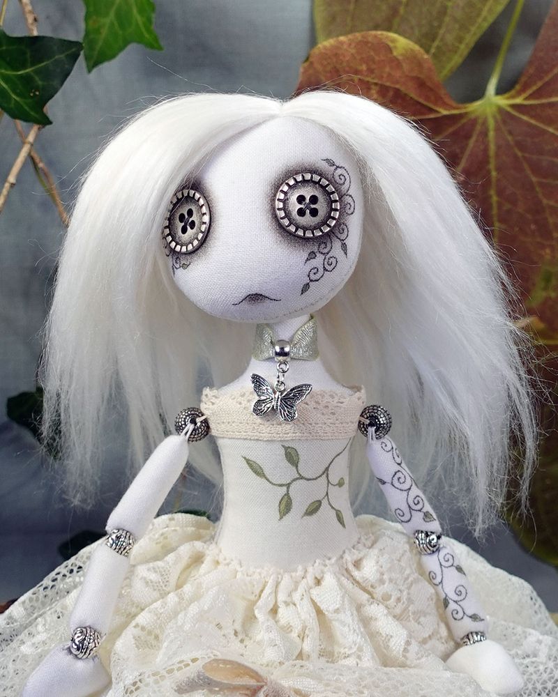 close up of button eyed ghost doll with hand painted vine detail and butterfly necklace