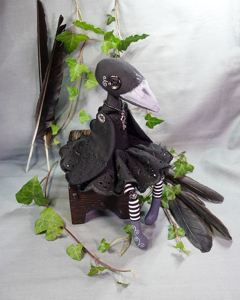 a crow art doll in black dress with key necklace and silver buttons on wings