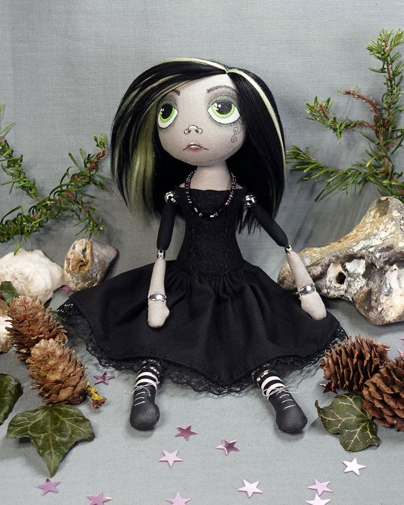 a cloth art doll in black dress with large eyes and sad face