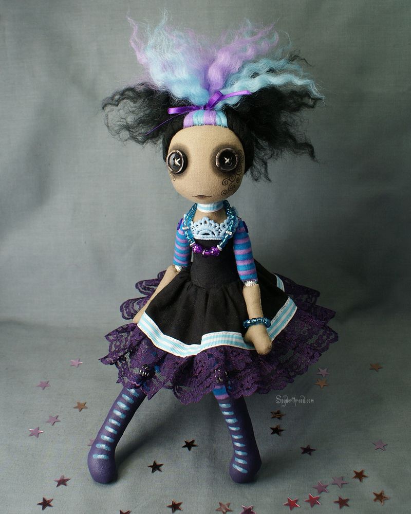 a button eyed art doll with tan skin dressed in black purple and blue