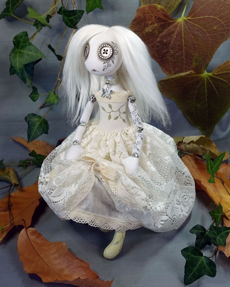 a button eyed ghost art doll with long white hair and ivory lace dress with hand painted vine detail