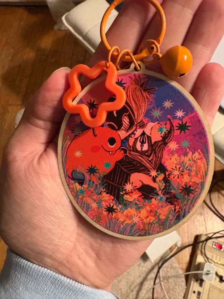 Wooden charm of reze and pochita with a orange claps and a bell and star shaped embellishment 