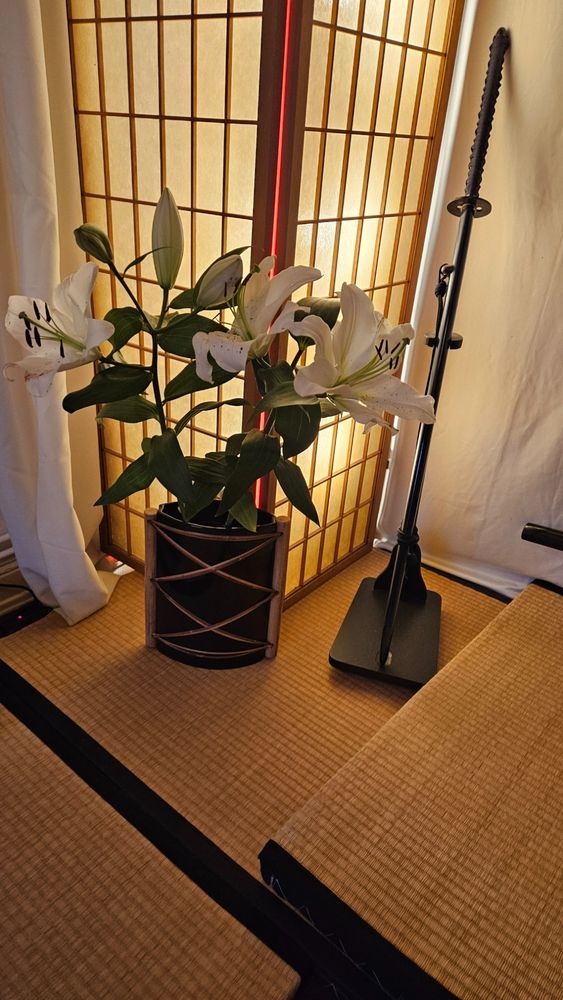 Lilien in schwarzer Vase, neben einem Katana und vor einem Paravent