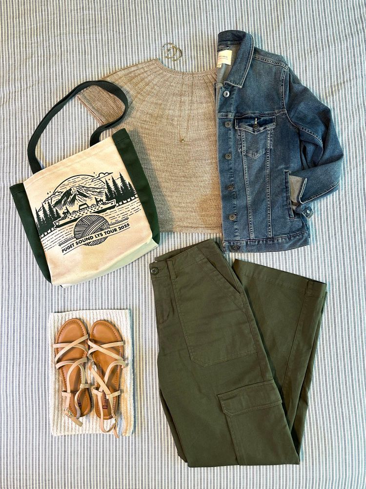 Flat lay of Sunday Tee with Universal Thread Cargo pants, Two by Vince Camuto jean jacket, strappy nude sandals, and Puget Sound LYS Tour 2025 tote bag