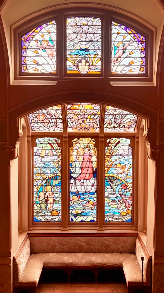 Gebrandschilderde ramen in de villa Rams Woerthe. De villa ligt in Steenwijk, Overijssel. Op de afbeelding in het midden twee jonge vrouwen die door zwanen worden voortgetrokken. In het meer zwemmen cherubijnen, er zijn waterlelies, vissen, diverse waterplanten, een paar bootjes en in de verte contouren van een stad. Alles gemaakt in Jugendstil stijl, dus er zit veel beweging in de afbeelding. De kleuren zijn helder en sprankelend, zoals fel blauw, geel, oranje. De raampartij bestaat uit 3 grote rechthoeken met daarboven 3 kleinere meer ronde ramen. De raampartij zorgt voor het nodige licht voor de trappen, die van begane grond naar de eerste verdieping lopen. 