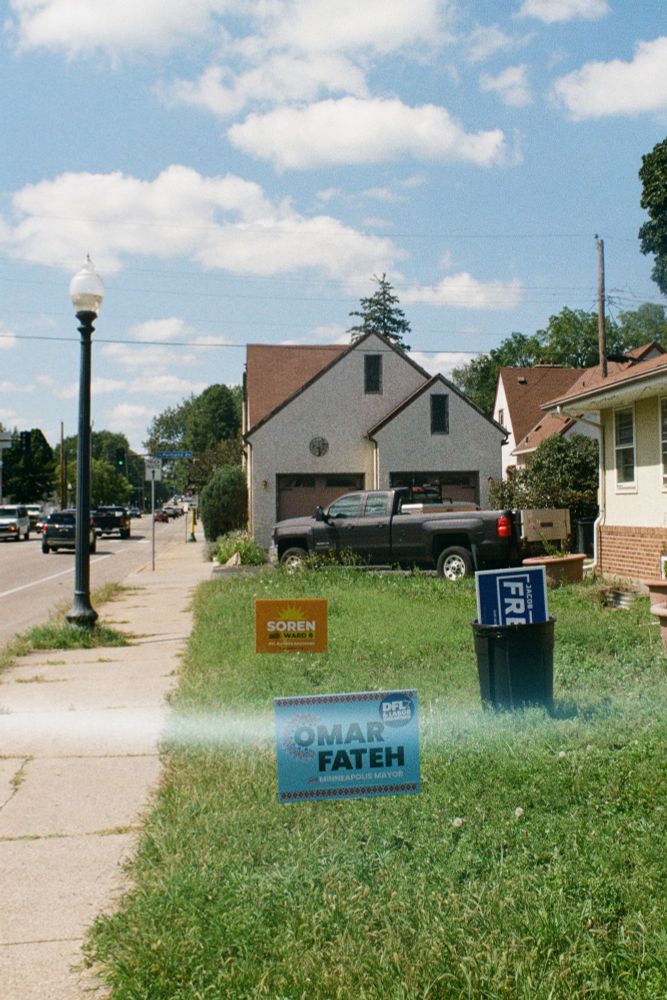 35mm photo of a Soren and Omar Fateh lawn sign paired with a Frey sign in a trash can. It is a summer day in Minneapolis, 2025