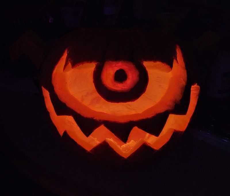 A lit pumpkin with a Final Fantasy Ahriman face carved into it.