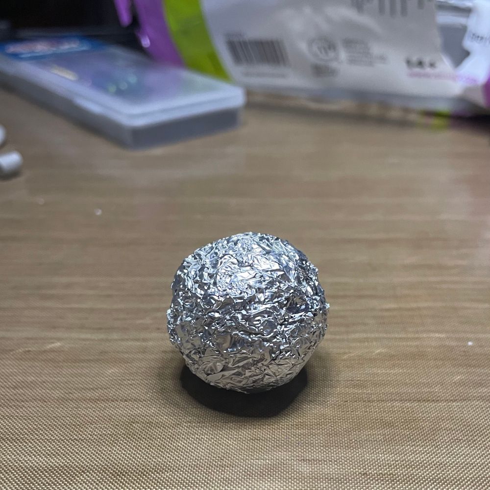 Ball of crumpled foil on a tan mat with clay and tools in the background.