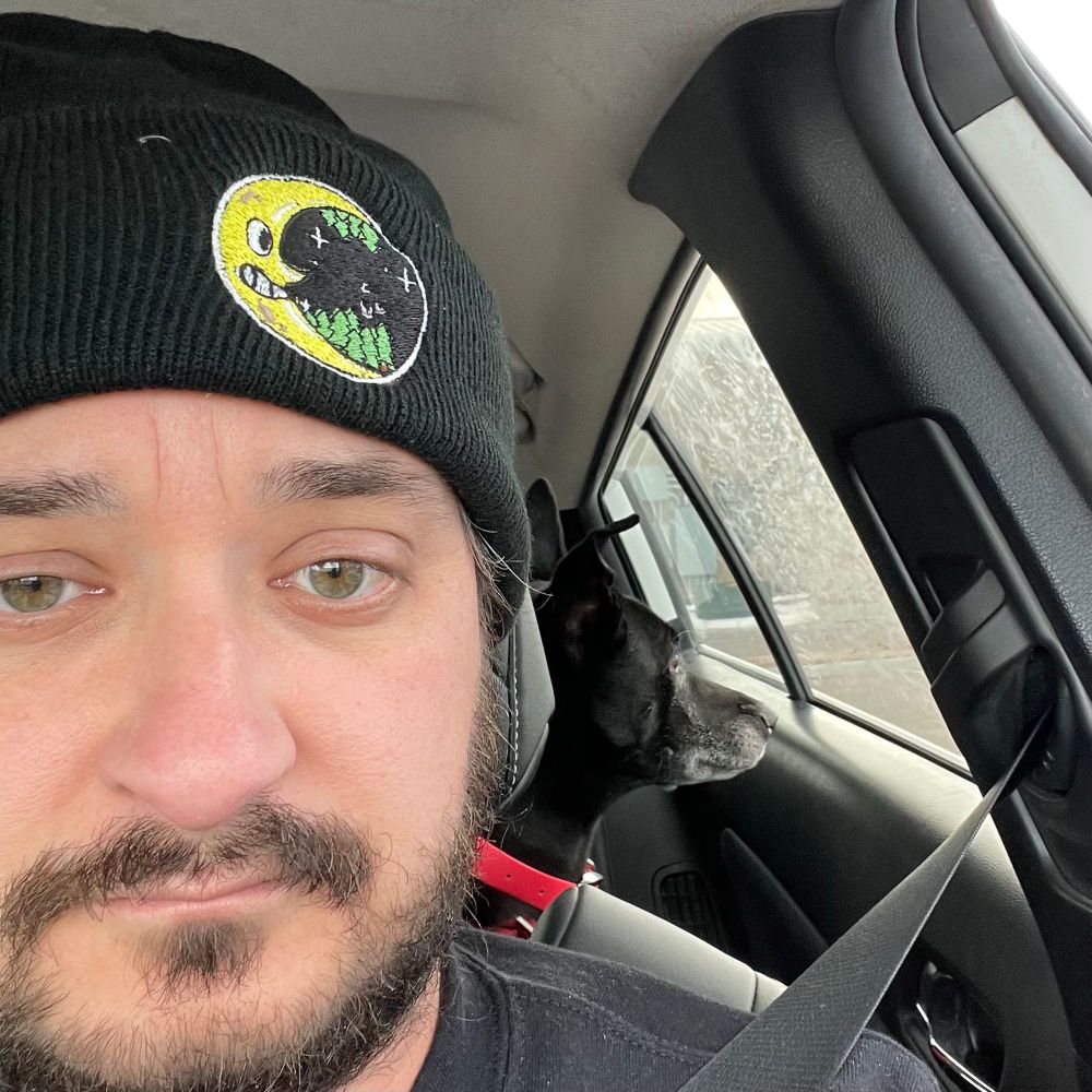 Me adult male face wearing beanie described in picture 1. I’m sitting in my car and with one of my dogs (black dog with a hot pink collar).